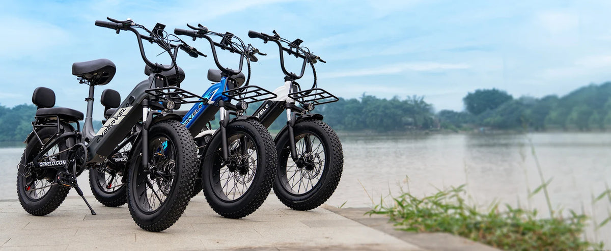 Four electric bikes parked by a body of water with trees in the background