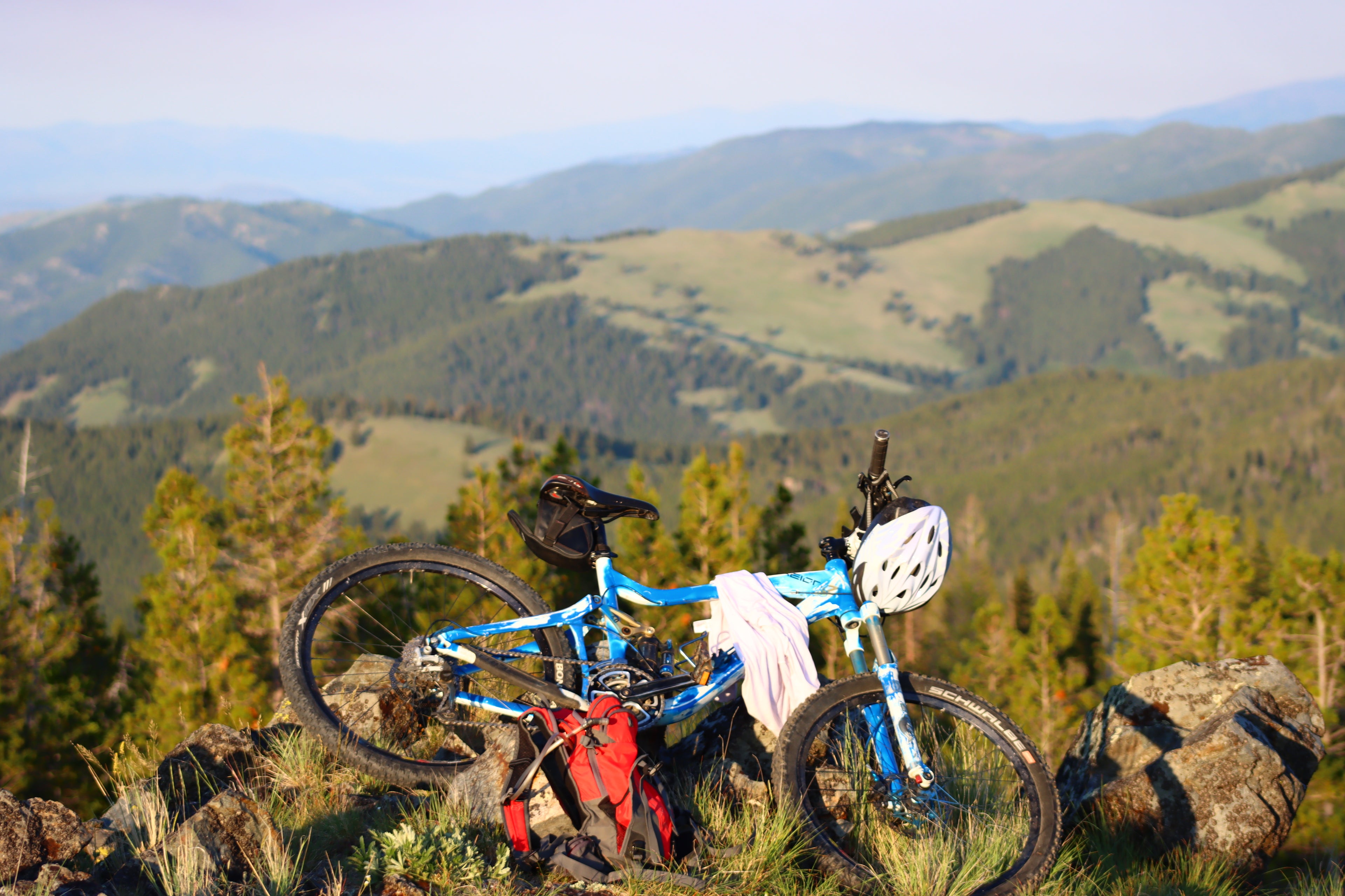 Blue mountain bike with a helmet and backpack on a rocky hilltop with mountains in the background